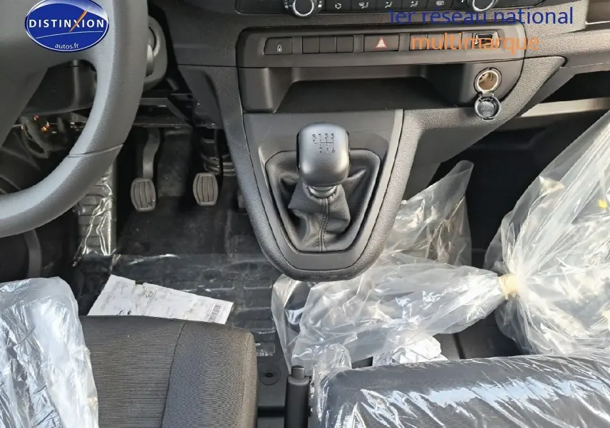 Gros plan sur la console centrale et levier de vitesse manuel du Peugeot Expert blanc, avec sièges noirs protégés par des housses plastiques.