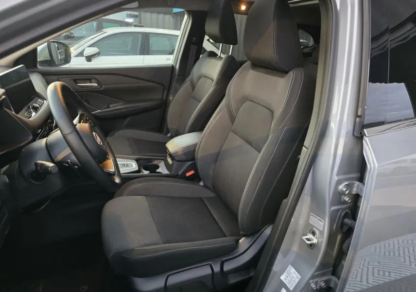 Intérieur avant du Nissan Qashqai gris silver 2024, sièges tissu noirs et accoudoir central visible côté conducteur.