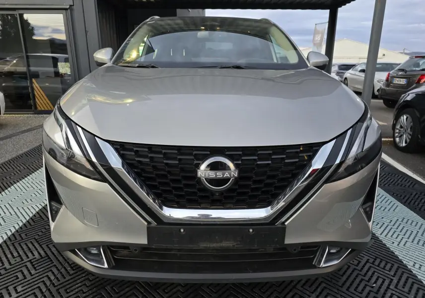Vue frontale d'un Nissan Qashqai gris silver 2024 avec calandre noire et détails chromés sous un abri.