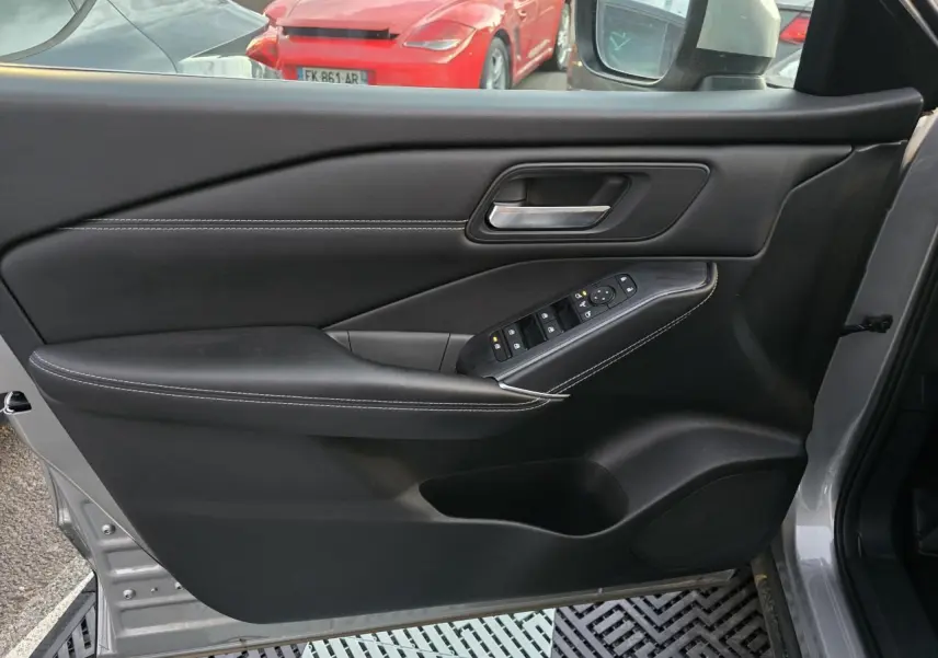 Vue intérieure côté gauche de la porte avant gris silver du Nissan Qashqai 2024 avec commandes de vitres et poignée intégrée.
