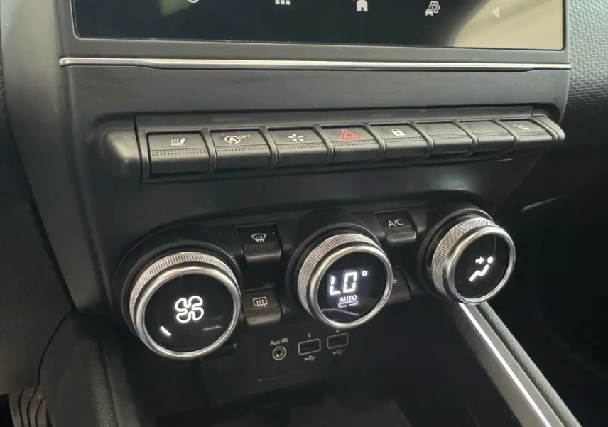 Gros plan sur la console centrale noire de la Renault Clio Intens 2020, montrant les commandes de climatisation et boutons multifonctions.