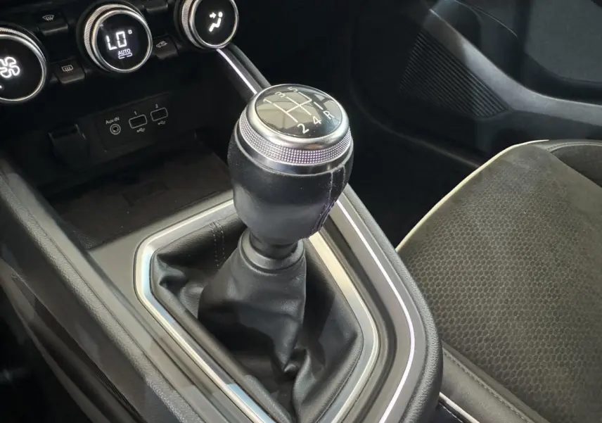 Gros plan sur le levier de vitesses manuel noir de la Renault Clio Intens 2020 avec console et siège tissu gris.