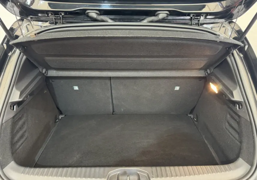 Coffre ouvert vu de l'arrière d'une Renault Clio Intens TCe 100 noire, montrant l'espace de chargement vide et la lumière intérieure.