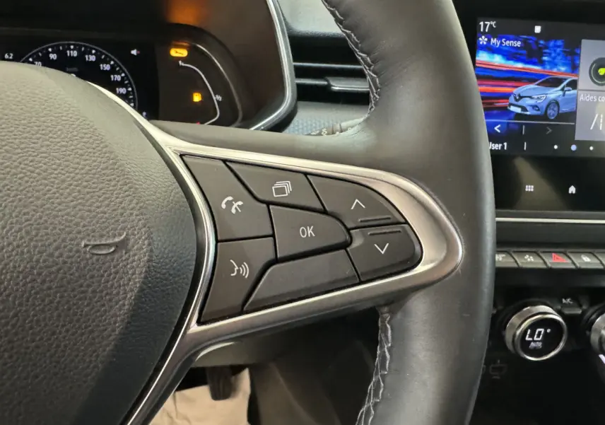 Gros plan sur les commandes droite du volant cuir de la Renault Clio Intens TCe 100 2020 avec écran tactile et tableau de bord partiel.