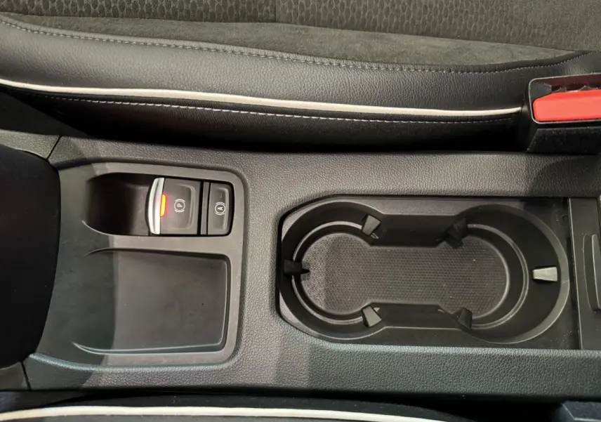 Gros plan sur la console centrale noire de la Renault Clio Intens TCe 100, avec frein à main électrique et porte-gobelets.
