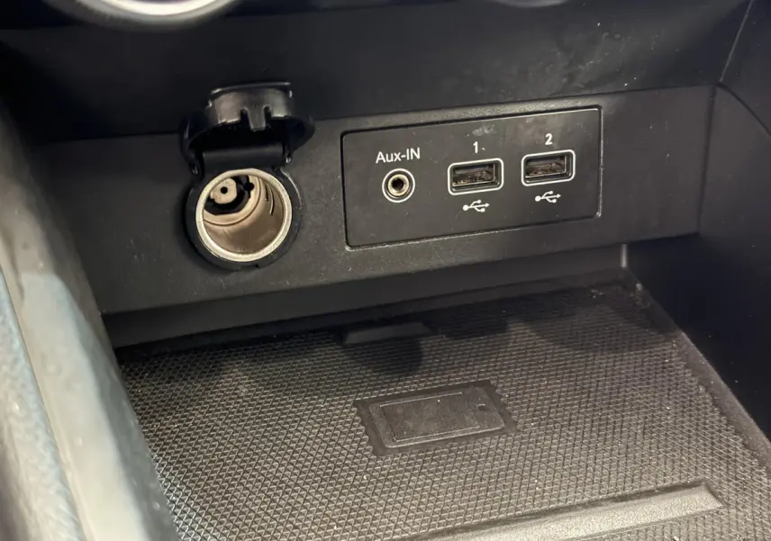 Vue rapprochée de la prise auxiliaire, deux ports USB et allume-cigare dans la console centrale d'une Renault Clio Intens noire 2020.