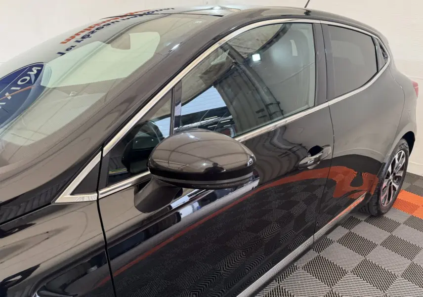 Vue latérale côté gauche d'une Renault Clio Intens TCe 100 noire, mettant en valeur la poignée et le rétroviseur extérieur.