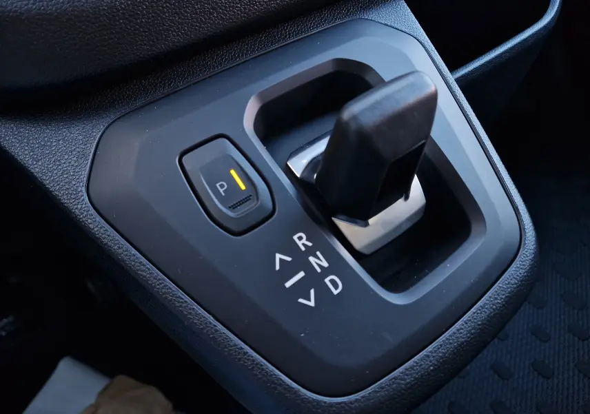 Gros plan sur le levier de vitesses automatique noir du Renault Trafic Fourgon blanc, avec bouton de parking activé.