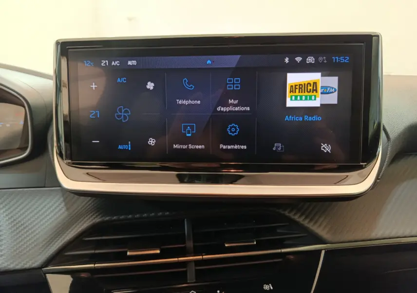 Écran tactile central affichant les commandes multimédia et climatisation dans une Peugeot 208 gris clair, vue intérieure frontale.