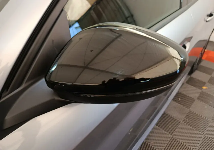 Rétroviseur noir côté gauche d'une Peugeot 208 gris clair, vue rapprochée en intérieur showroom.