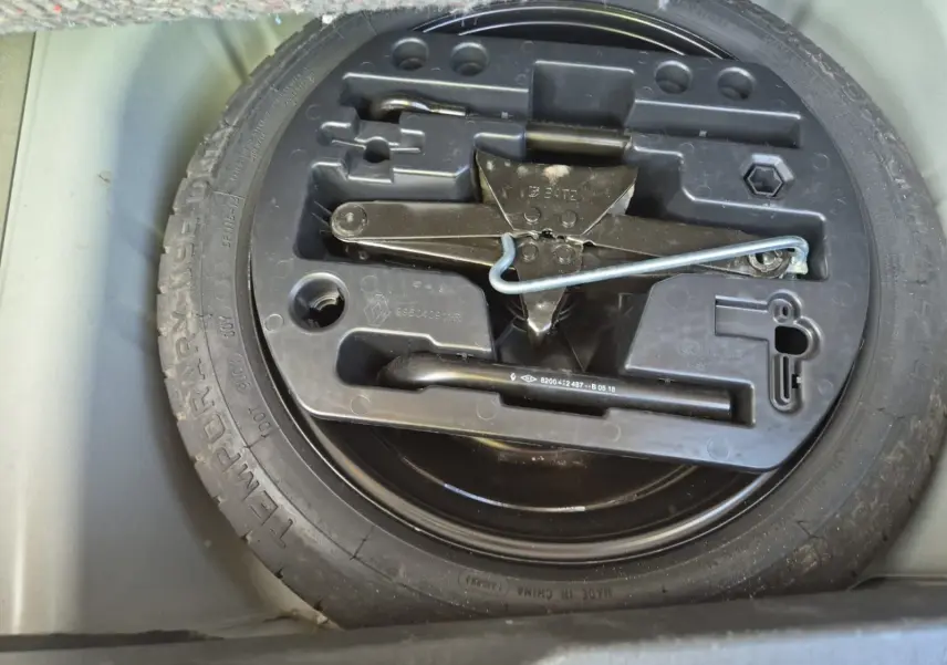 Gros plan sur la roue de secours et le cric noir dans le coffre du Renault Captur beige/marron 2018.