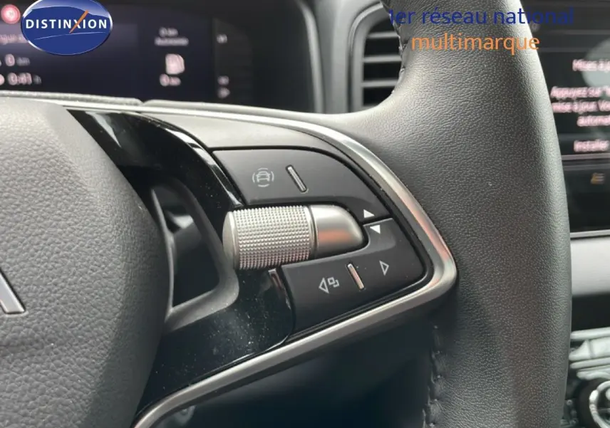 Gros plan sur les commandes multifonctions du volant en cuir noir du Skoda Karoq blanc glacier, avec tableau de bord en arrière-plan flou.