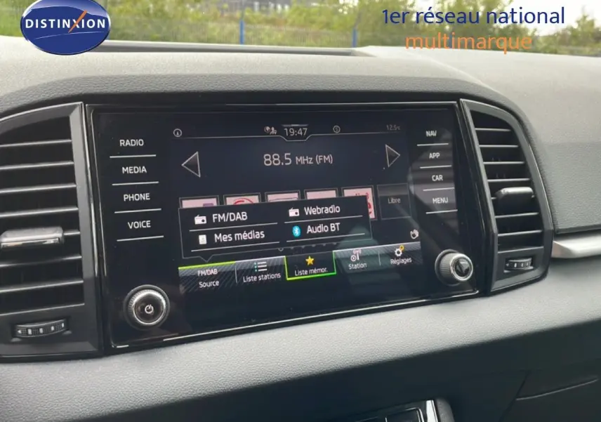 Écran tactile central du tableau de bord du Skoda Karoq blanc glacier, avec interface radio FM/DAB affichée.