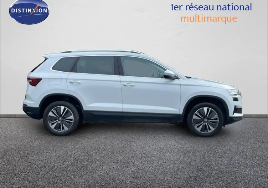 Vue profil droit d’un Skoda Karoq blanc glacier 2025 avec jantes alliage et barres de toit noires.