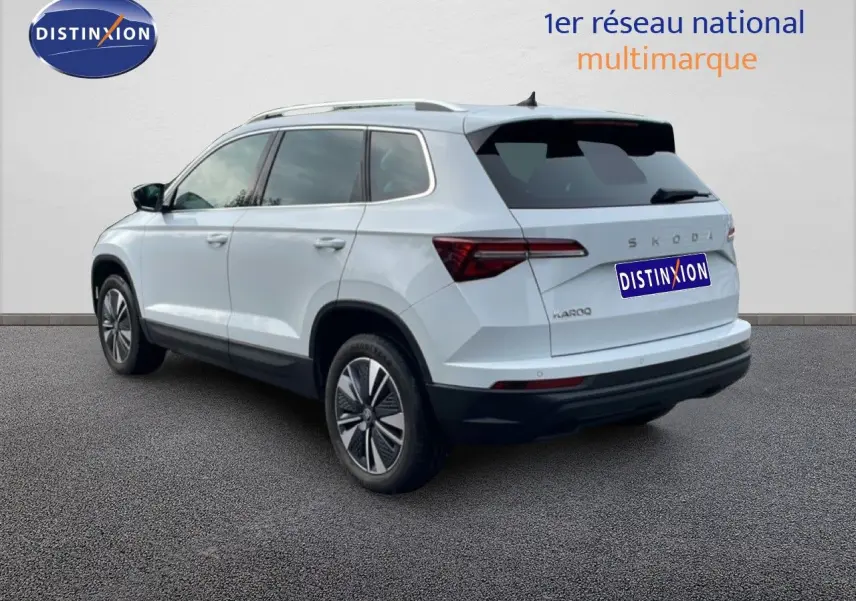Vue 3/4 arrière droite d’un Skoda Karoq blanc glacier avec jantes bi-ton et vitres teintées.