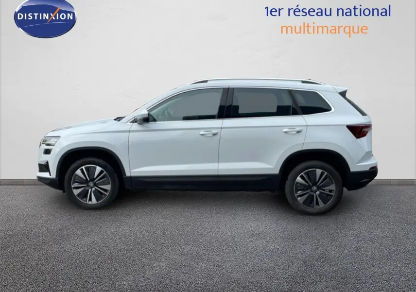Vue de profil côté gauche d’un Skoda Karoq blanc glacier 2025 avec jantes bi-ton et barres de toit noires.