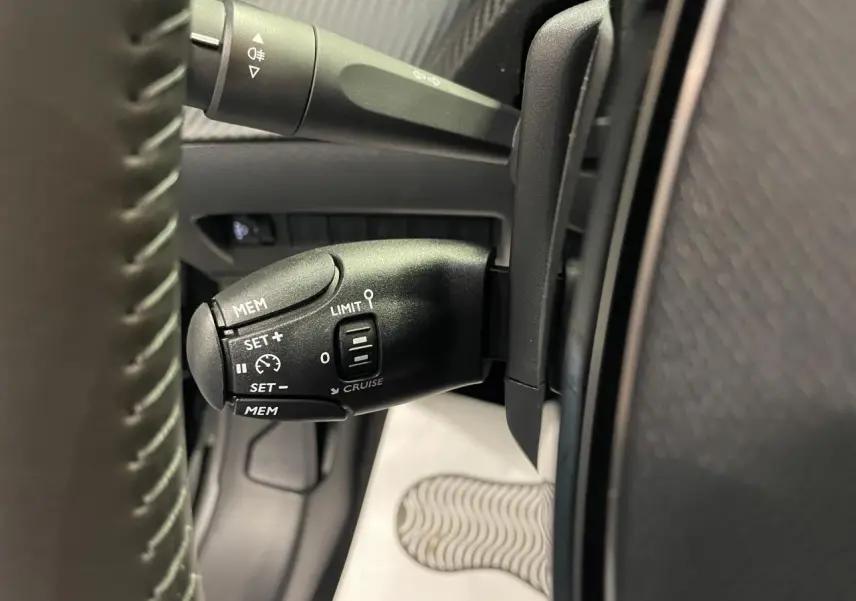 Gros plan sur la commande de régulateur de vitesse noire à gauche du volant dans l’habitacle d’une Peugeot 208 noire.