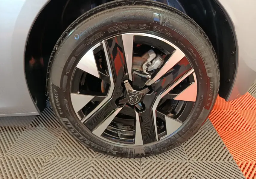 Gros plan sur la roue avant droite de la Peugeot 208 gris clair avec jante alliage noire et argentée au design moderne.