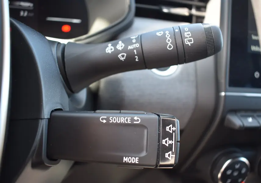 Gros plan sur les commandes au volant à gauche de la Renault Clio V noire, mettant en valeur les boutons source et mode.