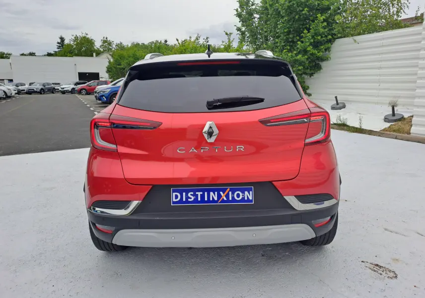 Vue arrière d'un Renault Captur rouge flamme métal 2024 avec feux LED et logo distinctif sur un parking.
