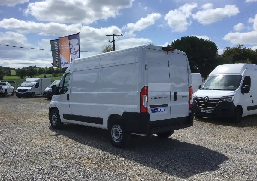 Fourgon Peugeot Boxer blanc vu en 3/4 arrière droit sur un parking avec plusieurs véhicules utilitaires.
