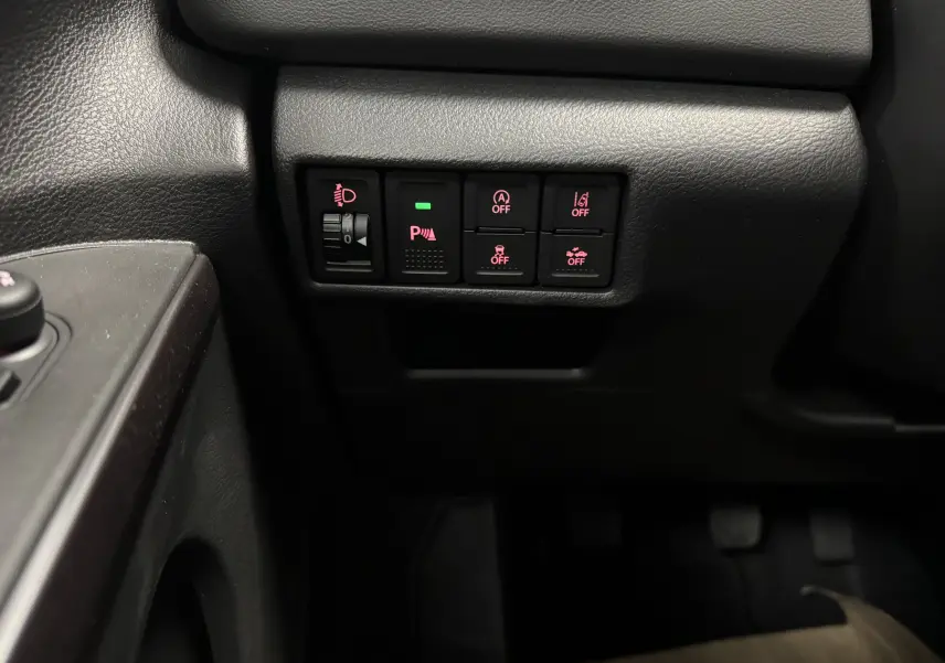 Gros plan sur les commandes de sécurité et d'assistance situées à gauche du conducteur dans le Suzuki S-Cross blanc 2025.