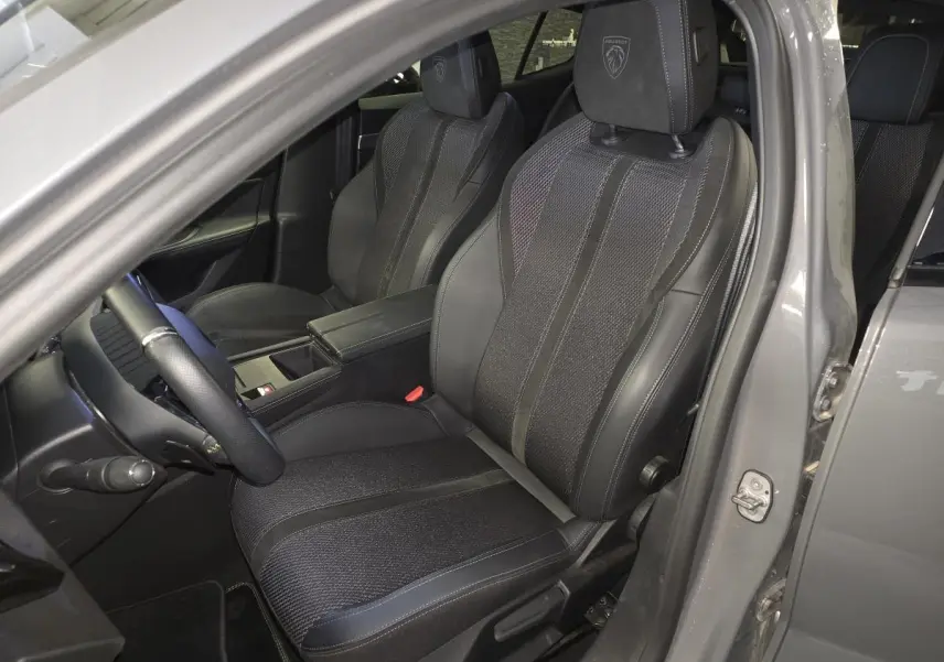 Vue intérieure côté conducteur du Peugeot 408 gris, mettant en valeur les sièges sport noirs avec logo Peugeot brodé sur les appuis-tête.