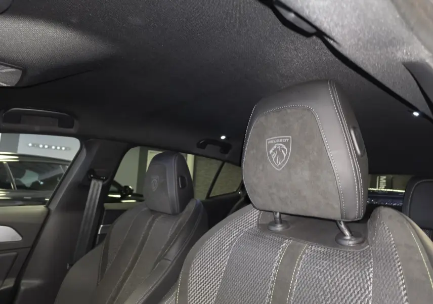Gros plan sur les sièges avant gris avec appuis-tête brodés du lion Peugeot dans l’habitacle sombre de la 408 GT 2025.