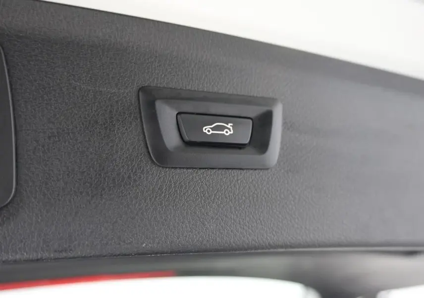 Gros plan sur le bouton d'ouverture électrique du hayon intérieur d'une BMW Série 2 Active Tourer blanche.