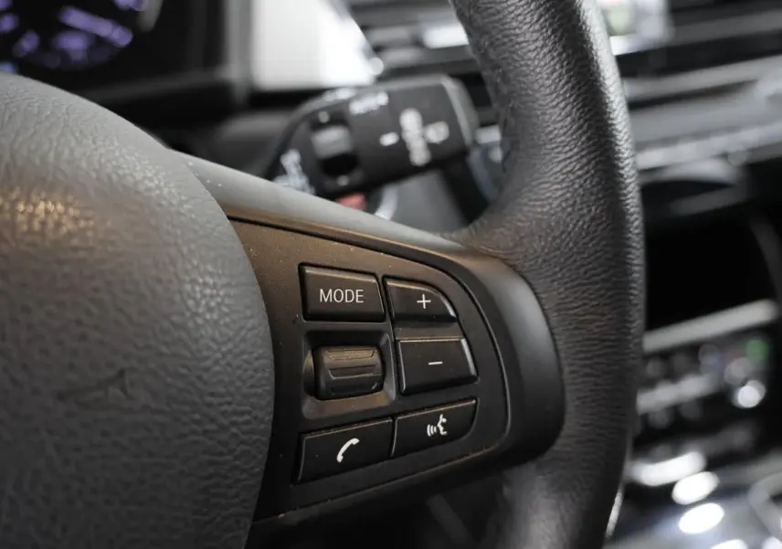 Gros plan sur les commandes multifonctions noires du volant en cuir de la BMW Série 2 Active Tourer 216d.