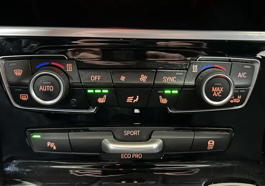 Gros plan sur la console centrale de la BMW Série 2 Active Tourer blanche, avec commandes climatisation et sièges chauffants activés.