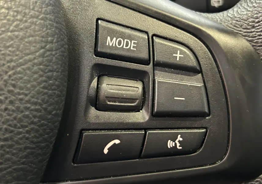 Gros plan sur les commandes multifonctions noires du volant d’une BMW Série 2 Active Tourer blanche de 2021.