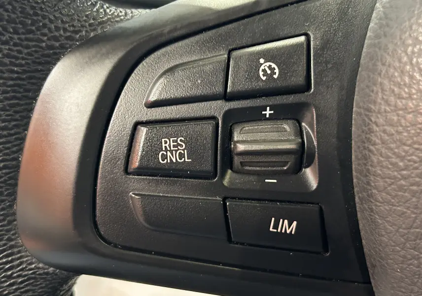 Gros plan sur les commandes de régulateur de vitesse au volant noir du BMW Série 2 Active Tourer blanc.