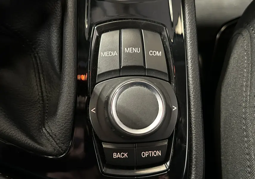 Gros plan sur la molette de commande centrale noire avec boutons MEDIA, MENU, COM, BACK et OPTION dans une BMW Série 2 Active Tourer.
