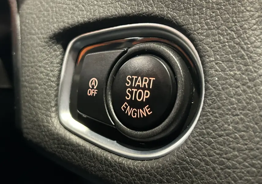 Gros plan sur le bouton Start Stop Engine noir entouré de cuir noir texturé à l'intérieur d'une BMW Série 2 Active Tourer blanche.
