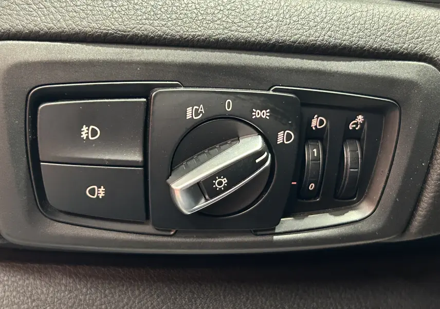Gros plan sur le bouton de commande des phares d'une BMW Série 2 Active Tourer blanche, intérieur noir.