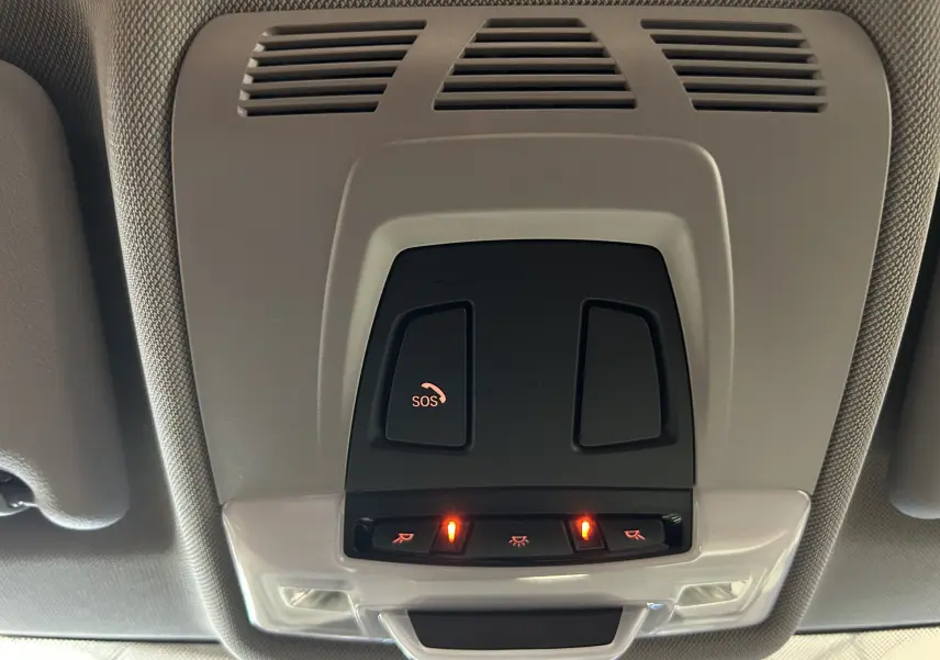 Vue en gros plan du panneau de commandes au plafond intérieur de la BMW Série 2 Active Tourer blanc, avec bouton SOS et éclairage activé.