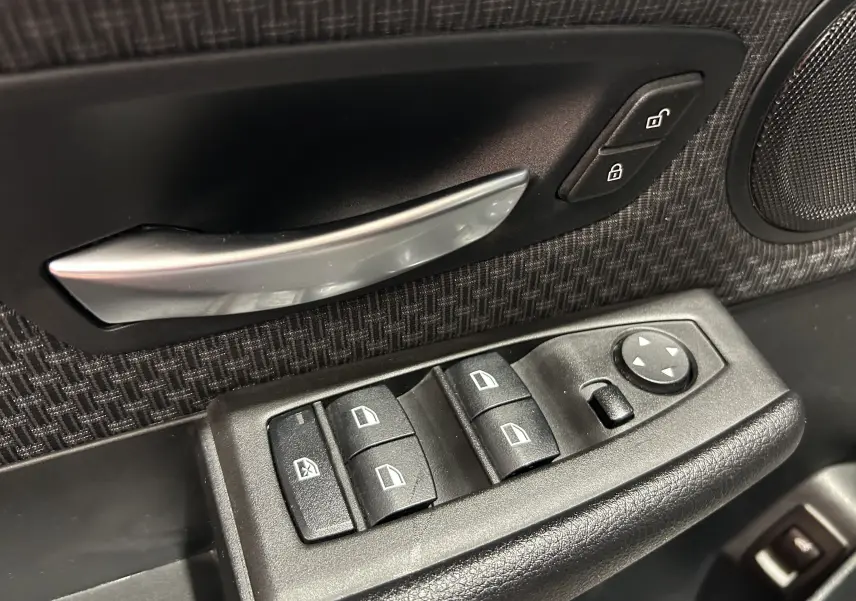 Gros plan sur la commande de lève-vitres et la poignée intérieure côté conducteur d’une BMW Série 2 Active Tourer 216d blanche.