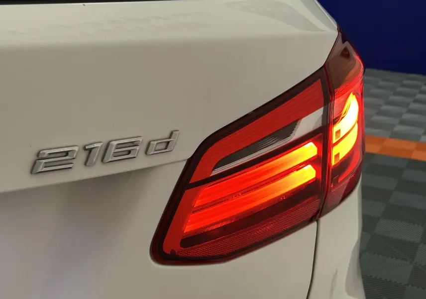 Gros plan sur le feu arrière droit allumé et l’inscription 216d sur la partie arrière blanche d’une BMW Série 2 Active Tourer.