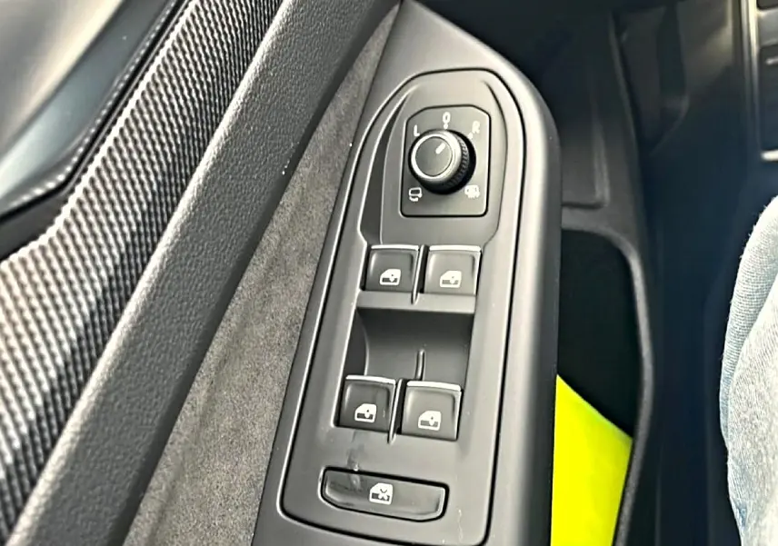 Gros plan sur les commandes de réglage des rétroviseurs et vitres côté conducteur d'une Volkswagen Golf noire 2026.