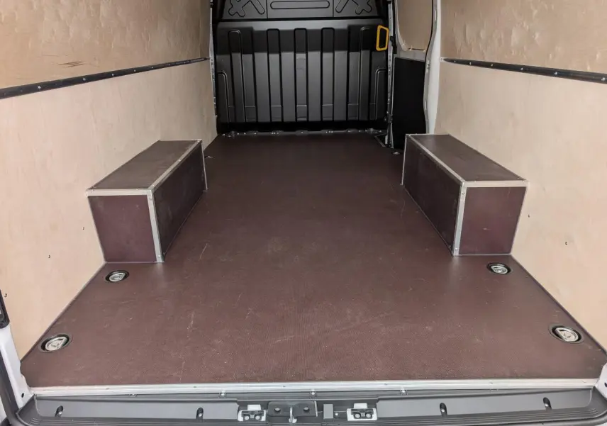 Vue intérieure arrière du fourgon blanc Iveco Daily 35S16 avec plancher antidérapant marron et habillages bois clairs.