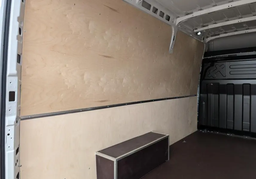 Intérieur du coffre du fourgon Iveco Daily blanc, vue latérale gauche avec habillage bois et plancher antidérapant.
