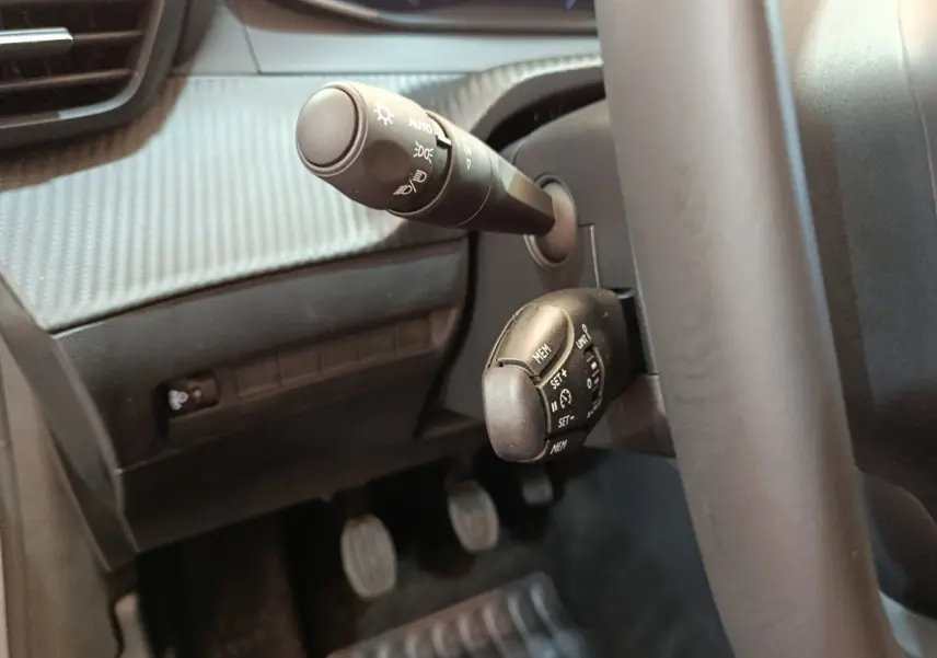 Gros plan sur commandes au volant et levier d'éclairage dans l'habitacle gris foncé d'une Peugeot 208 PureTech 100 S&S Allure