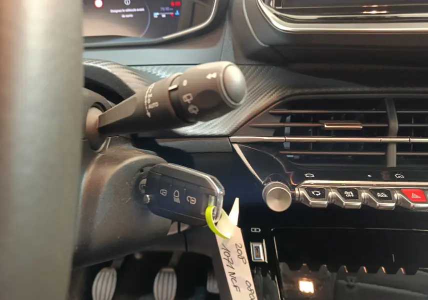 Gros plan intérieur côté gauche sur le tableau de bord et clé insérée d'une Peugeot 208 gris clair 2025 PureTech Allure