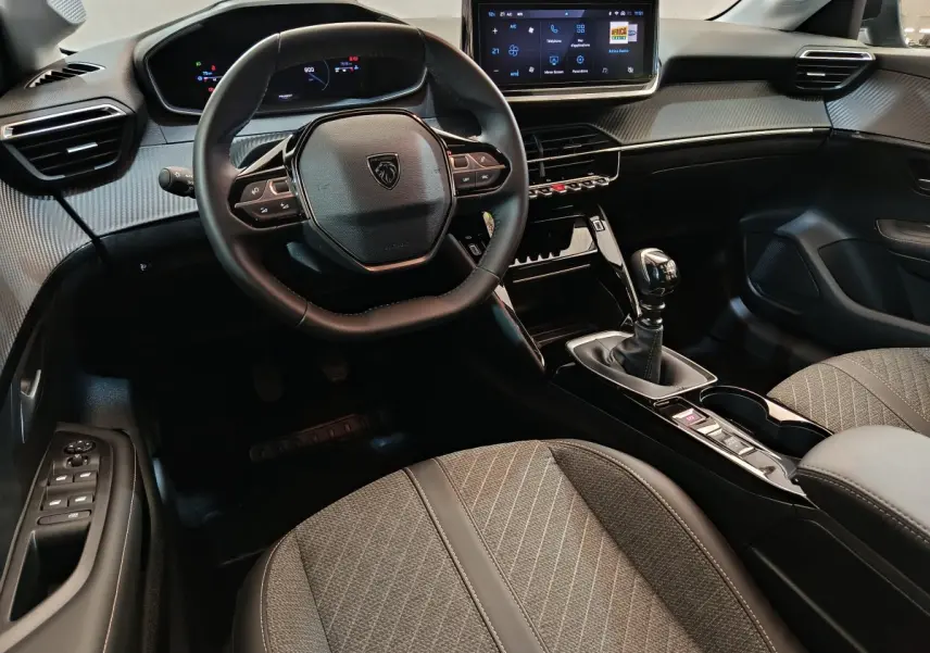 Vue intérieure avant de la Peugeot 208 gris clair, volant cuir, écran tactile central et boîte manuelle visible.