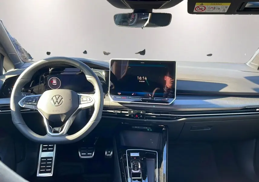 Vue intérieure avant de la Volkswagen Golf noire 2026, avec volant multifonction, écran tactile central et pédalier sport en aluminium.