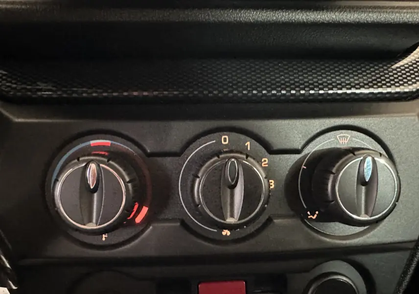 Gros plan sur les commandes de climatisation noires d'une Aixam Ambition rouge, avec réglages de température, ventilation et désembuage.