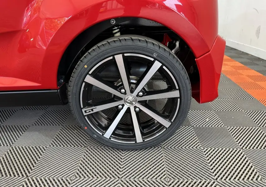 Gros plan sur la roue arrière droite rouge d'une Aixam Ambition 0.5 City Coupe GTI avec jante noire et argentée GT.
