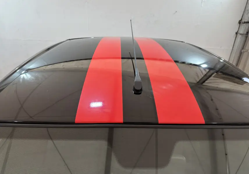 Vue en plongée du toit noir de l'AIXAM AMBITION 0.5 City Coupe GTI rouge avec deux bandes rouges centrales et antenne.