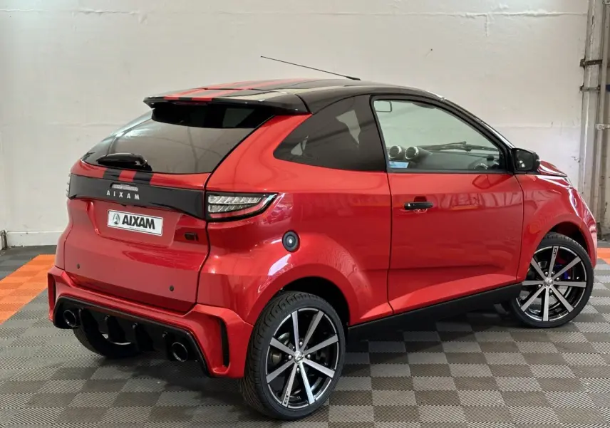 Vue 3/4 arrière droite de l'AIXAM AMBITION 0.5 CITY COUPE GTI rouge avec toit noir et jantes sport.